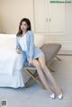 A woman sitting on a bed wearing a blue suit and white shoes.