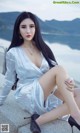 A woman in a silver dress sitting on a ledge by the water.