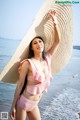 A woman in a pink bikini and a straw hat on the beach.