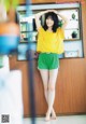 A woman in a yellow shirt and green shorts posing for a picture.