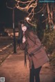 A woman in a brown coat standing on a sidewalk at night.