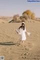 A woman in a white dress is walking in the sand.