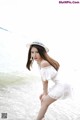 A woman in a white dress and hat posing on the beach.