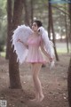 A woman in a pink dress with white wings standing in the woods.