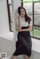 A woman sitting on a window sill wearing a black and white dress.