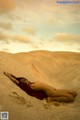 A naked woman laying on top of a sand dune.