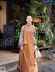 A woman standing in front of a flower shop wearing a brown dress.