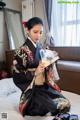 A woman in a kimono sitting on a bed holding a fan.