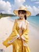 A woman in a yellow kimono and a straw hat on the beach.