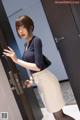 A woman in a blue shirt and white skirt is opening a door.