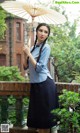 A woman in a blue shirt and black skirt holding an umbrella.